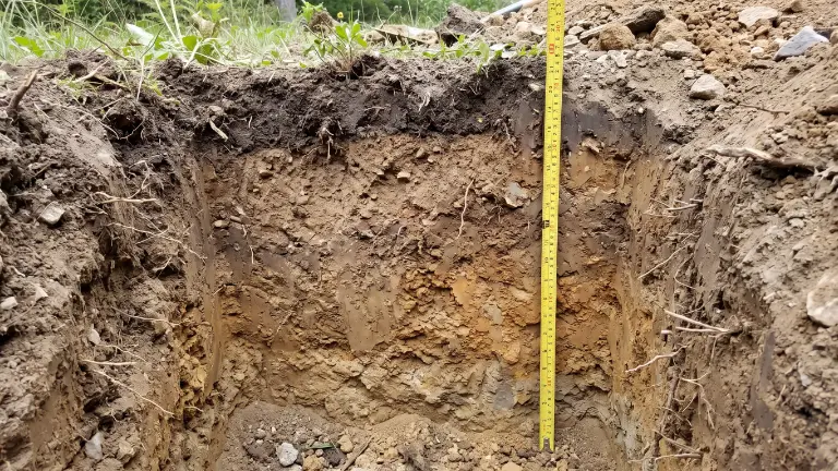 Soil profile exposed in a dug test pit, with a yellow tape measure marking the depth